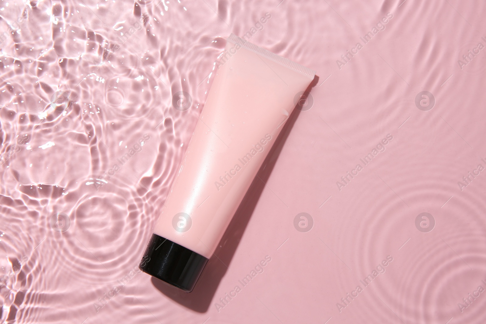 Photo of Cosmetic product. Tube with cream in water on pink background, top view