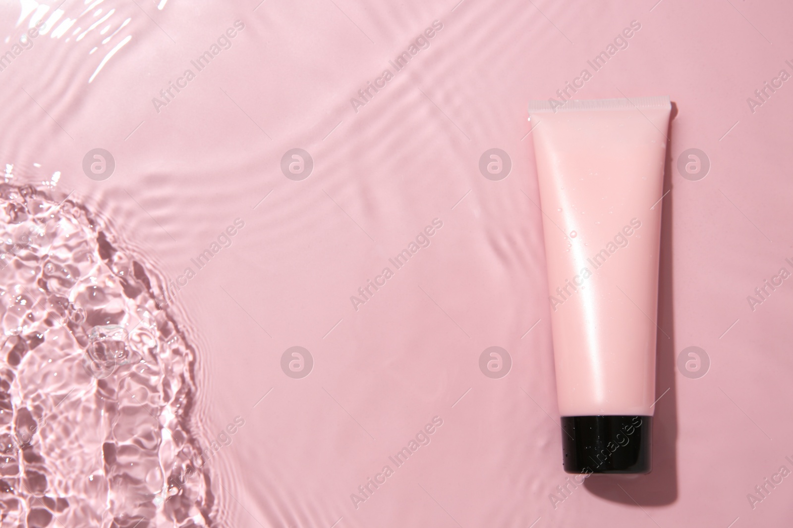 Photo of Cosmetic product. Tube with cream in water on pink background, top view. Space for text