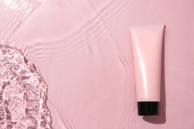 Cosmetic product. Tube with cream in water on pink background, top view. Space for text