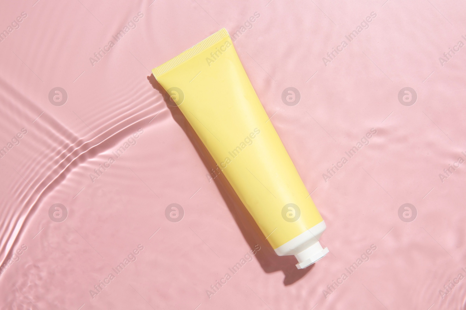 Photo of Cosmetic product. Tube with cream in water on pink background, top view