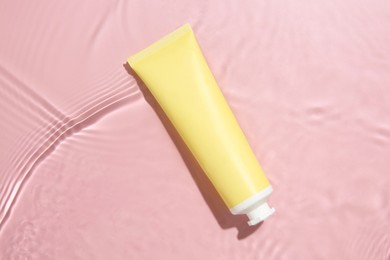 Cosmetic product. Tube with cream in water on pink background, top view