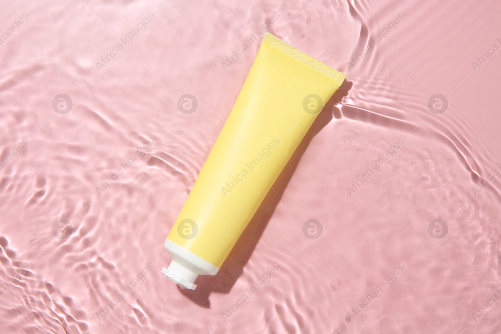 Photo of Cosmetic product. Tube with cream in water on pink background, top view