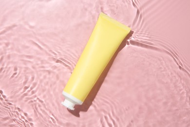 Cosmetic product. Tube with cream in water on pink background, top view