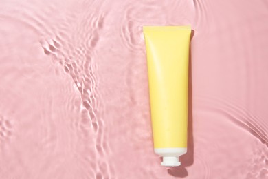 Cosmetic product. Tube with cream in water on pink background, top view. Space for text