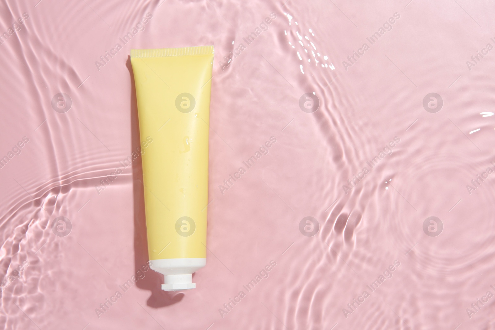 Photo of Cosmetic product. Tube with cream in water on pink background, top view. Space for text