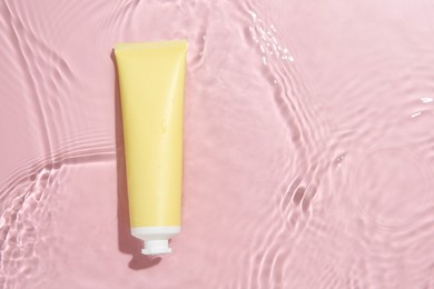 Cosmetic product. Tube with cream in water on pink background, top view. Space for text