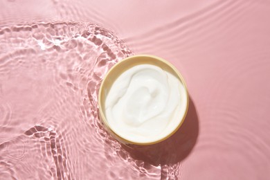 Photo of Cosmetic product. Jar with cream in water on pink background, top view