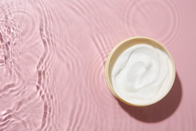 Cosmetic product. Jar with cream in water on pink background, top view. Space for text