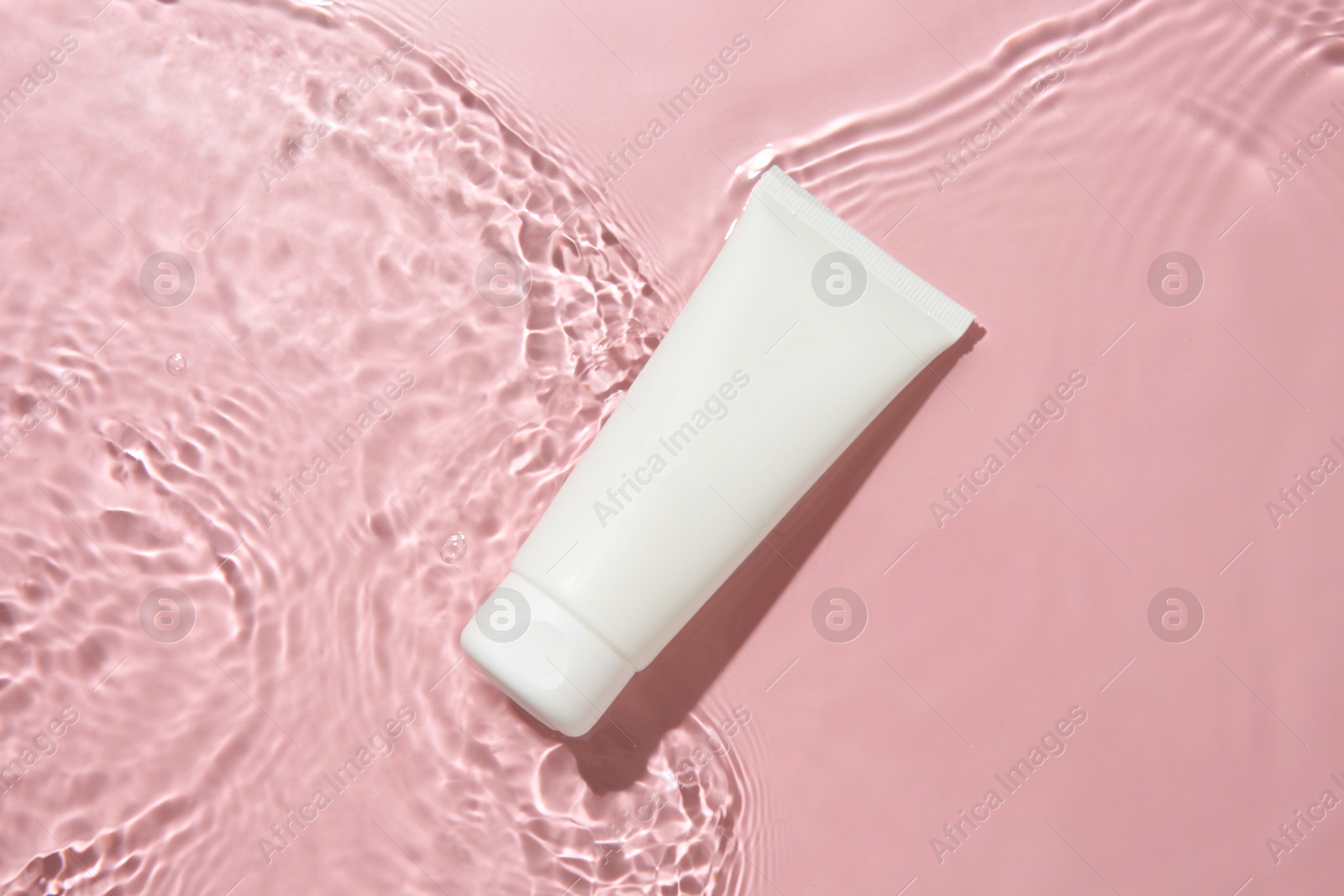 Photo of Cosmetic product. Tube with cream in water on pink background, top view