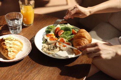 Photo of Woman having tasty breakfast at wooden table in cafe, closeup