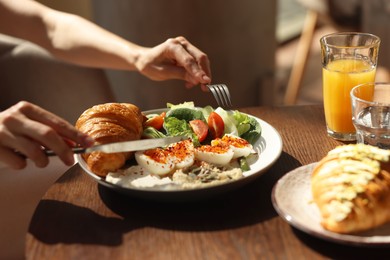 Woman having tasty breakfast at wooden table in cafe, closeup