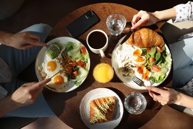 Photo of Couple having tasty breakfast at wooden table in cafe, top view