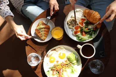 Photo of Couple having tasty breakfast at wooden table in cafe, top view