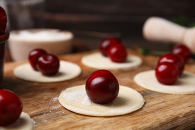 Photo of Process of making dumplings (varenyky) with cherries. Raw dough and ingredients on wooden table, closeup