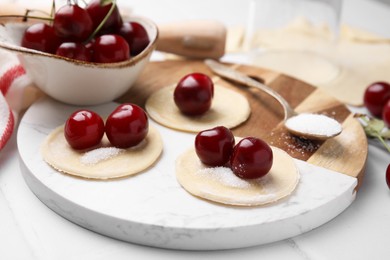 Process of making dumplings (varenyky) with cherries. Raw dough and ingredients on white tiled table, closeup