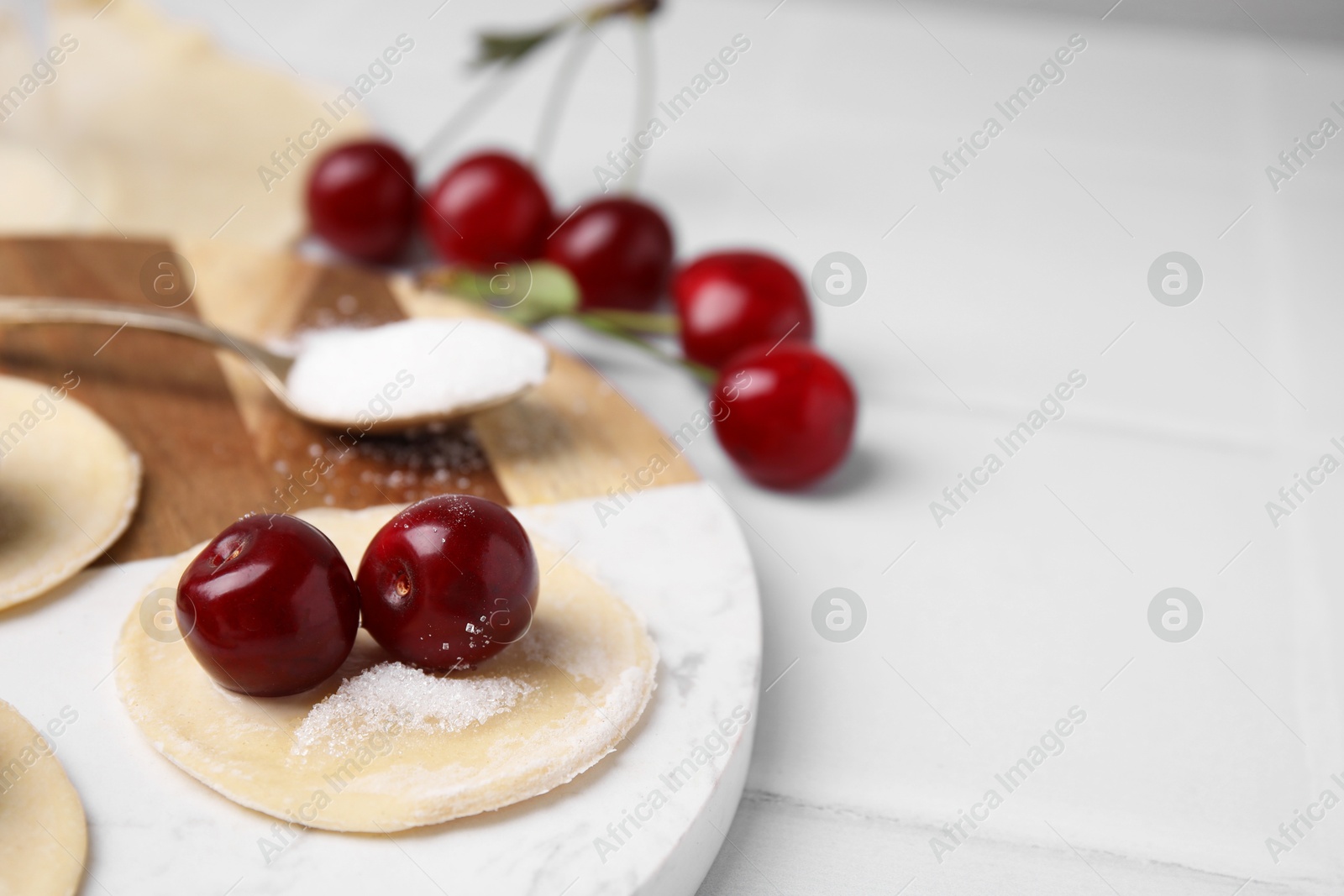 Photo of Process of making dumplings (varenyky) with cherries. Raw dough and ingredients on white tiled table, closeup. Space for text