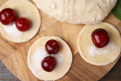 Process of making dumplings (varenyky) with cherries. Raw dough and ingredients on wooden table, top view