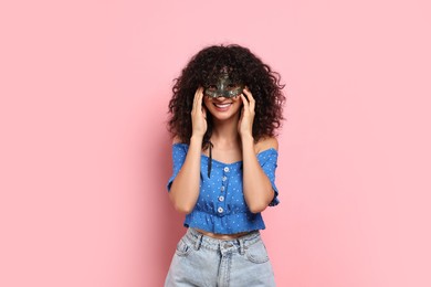 Photo of Happy young woman wearing carnival mask on pink background