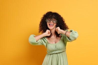 Photo of Happy young woman wearing carnival mask on yellow background