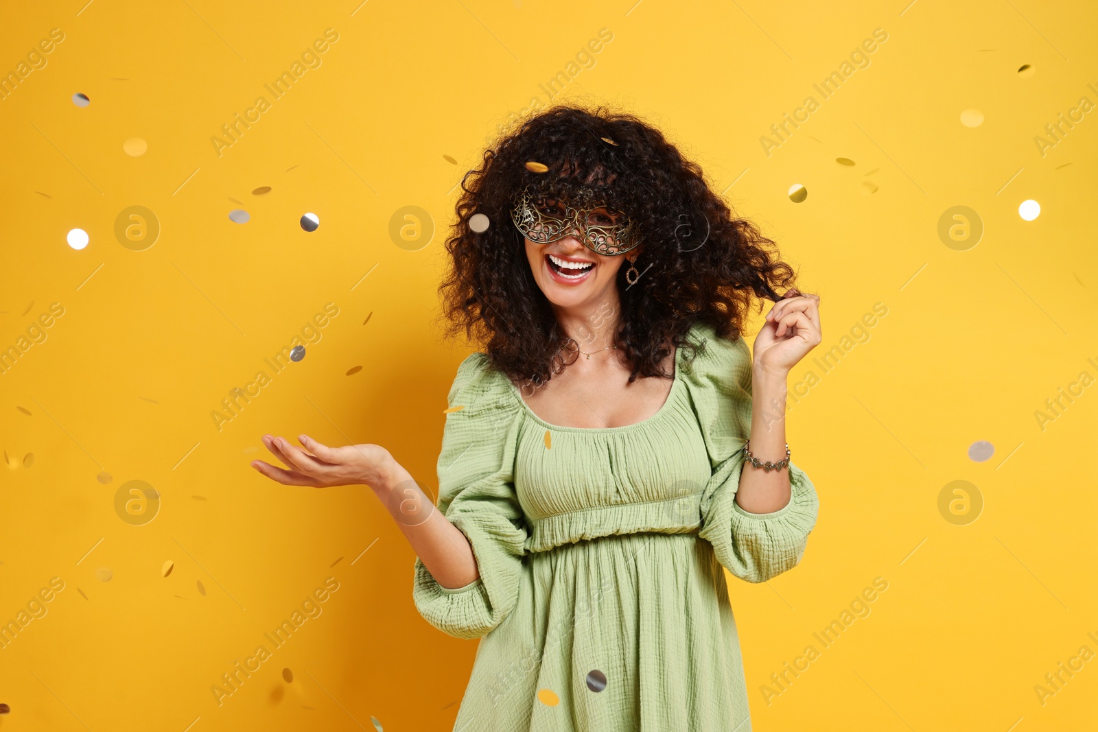 Photo of Happy young woman wearing carnival mask and confetti on yellow background