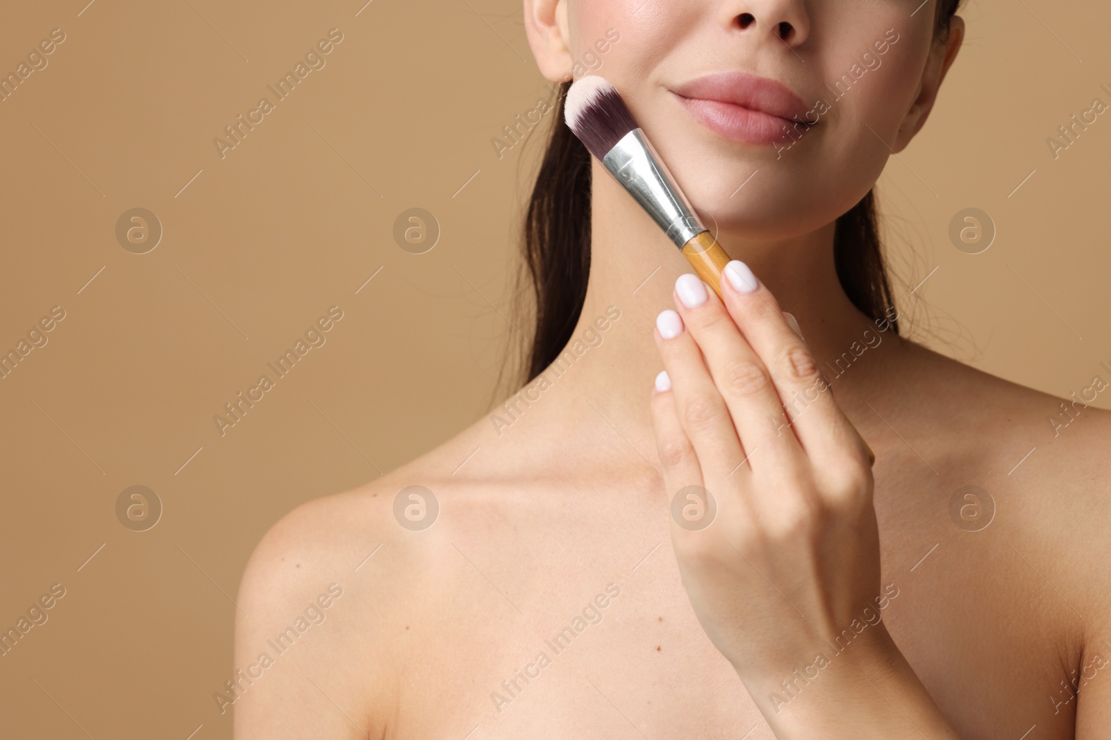 Photo of Woman applying makeup with brush on beige background, closeup. Space for text