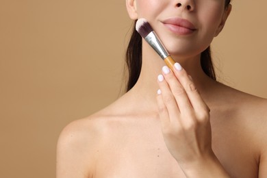 Woman applying makeup with brush on beige background, closeup. Space for text