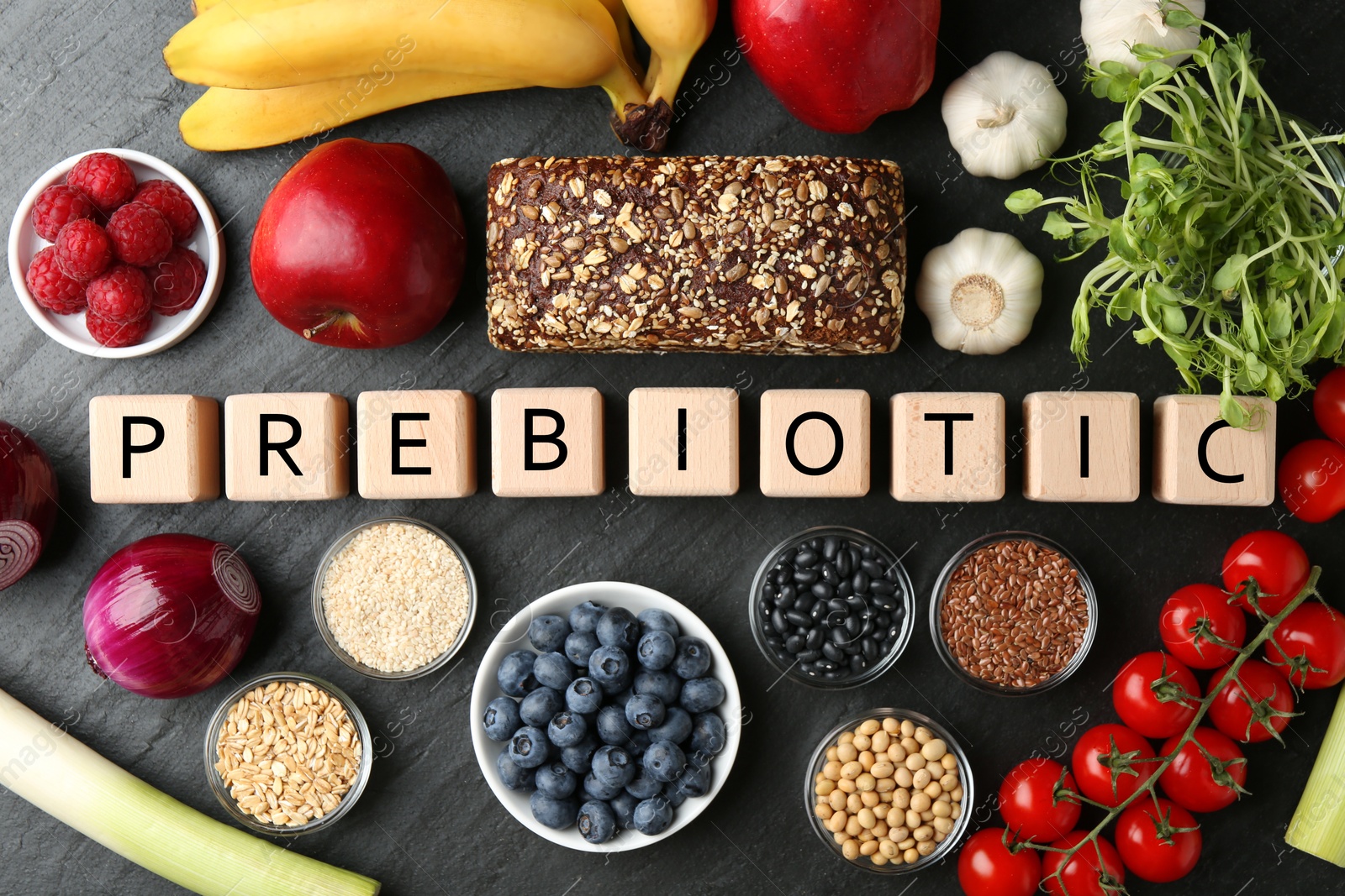 Photo of Wooden cubes with word Prebiotic and different fresh products on black table, flat lay