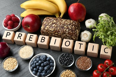 Photo of Wooden cubes with word Prebiotic and different fresh products on black table