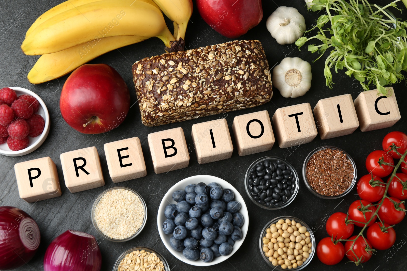 Photo of Wooden cubes with word Prebiotic and different fresh products on black table, flat lay