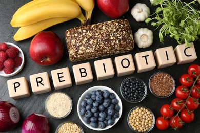 Photo of Wooden cubes with word Prebiotic and different fresh products on black table, flat lay