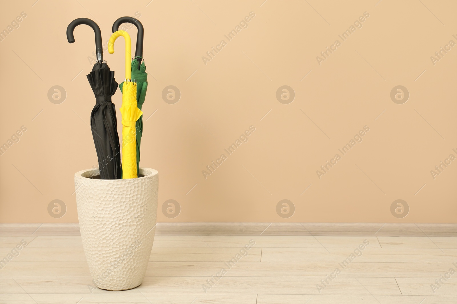 Photo of Colorful umbrellas in holder near beige wall indoors, space for text