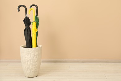 Photo of Colorful umbrellas in holder near beige wall indoors, space for text