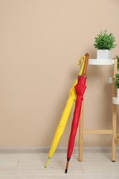 Photo of Colorful umbrellas and houseplants near beige wall, space for text