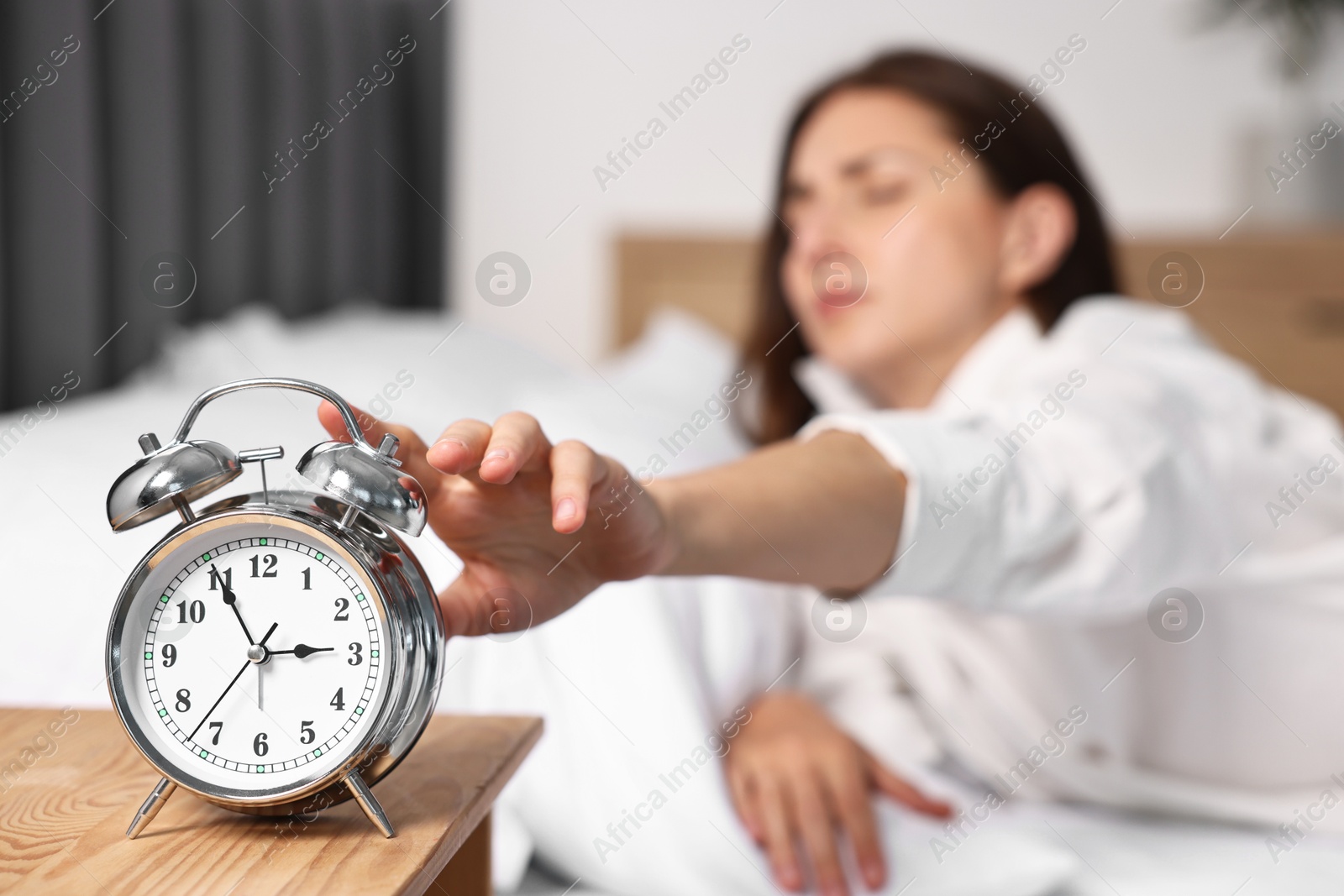 Photo of Woman turning off alarm clock in bedroom at lunch time, selective focus