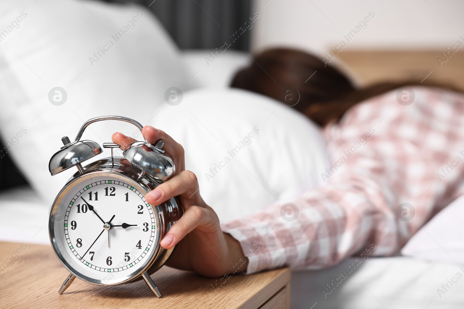 Photo of Woman turning off alarm clock in bedroom at lunch time, selective focus