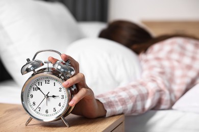 Woman turning off alarm clock in bedroom at lunch time, selective focus