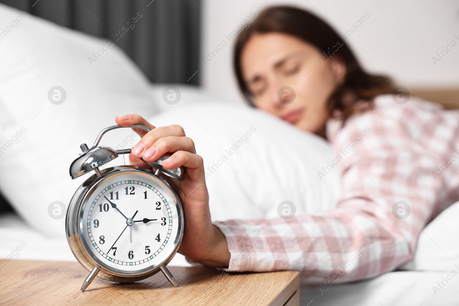 Photo of Woman turning off alarm clock in bedroom at lunch time, selective focus