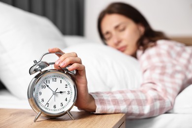 Woman turning off alarm clock in bedroom at lunch time, selective focus