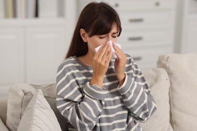 Photo of Woman with napkin suffering from sinusitis on sofa at home