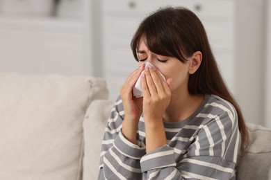 Woman with napkin suffering from sinusitis on sofa at home. Space for text