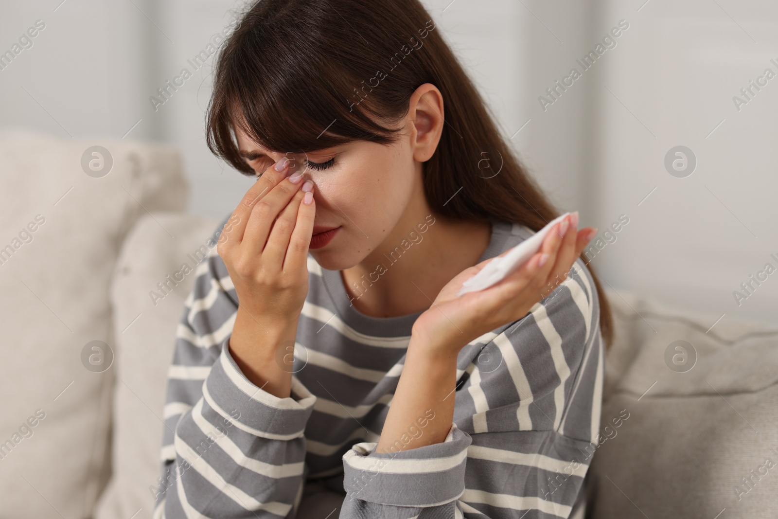 Photo of Woman with napkin suffering from sinusitis on sofa at home