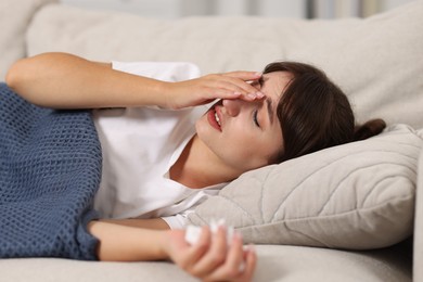 Photo of Woman with napkin suffering from sinusitis on sofa at home