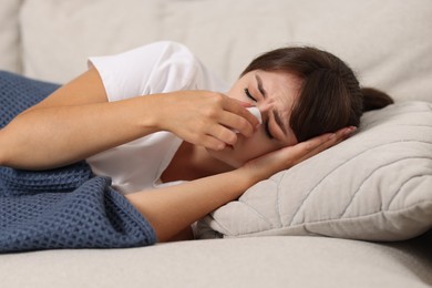 Photo of Woman with napkin suffering from sinusitis on sofa at home