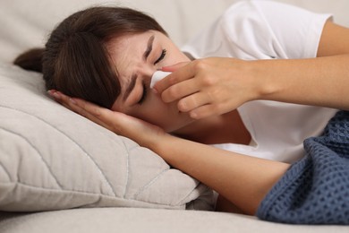 Photo of Woman with napkin suffering from sinusitis on sofa at home