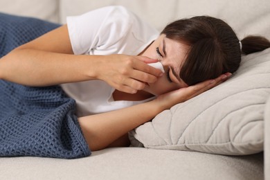 Woman with napkin suffering from sinusitis on sofa at home