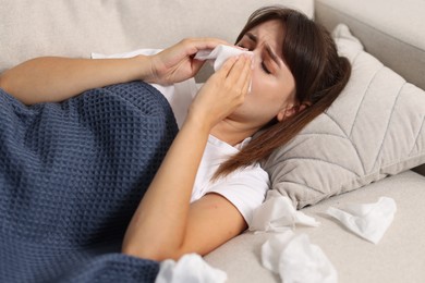 Photo of Woman with napkin suffering from sinusitis on sofa at home