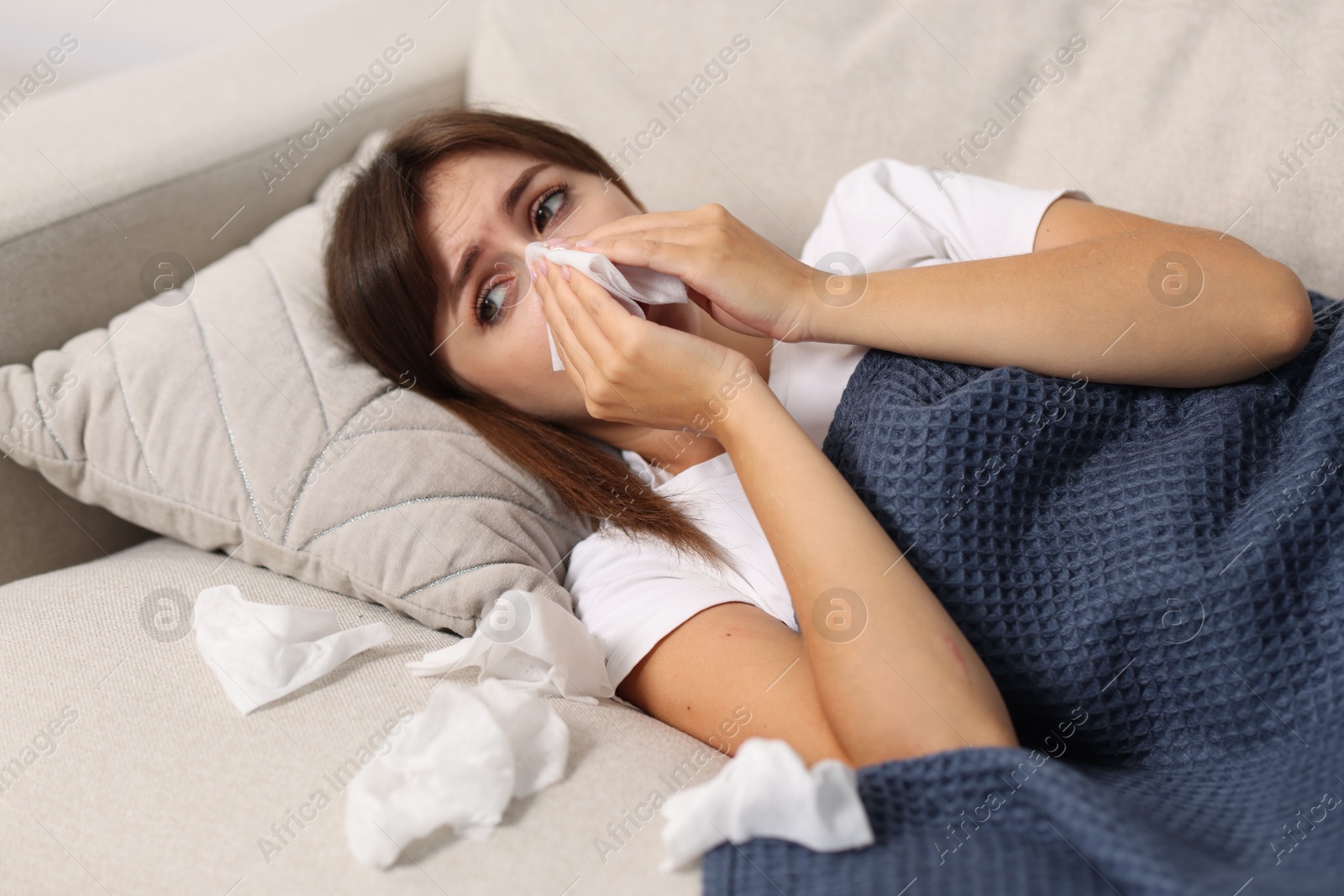 Photo of Woman with napkin suffering from sinusitis on sofa at home