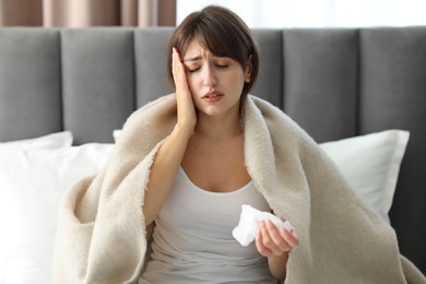 Woman wrapped in blanket suffering from sinusitis on bed