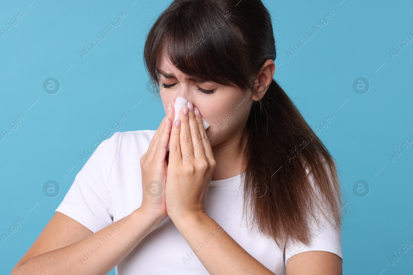 Photo of Woman with napkin suffering from sinusitis on light blue background