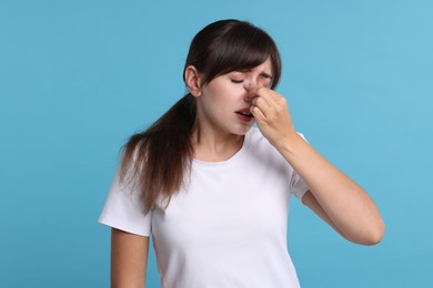 Woman suffering from sinusitis on light blue background